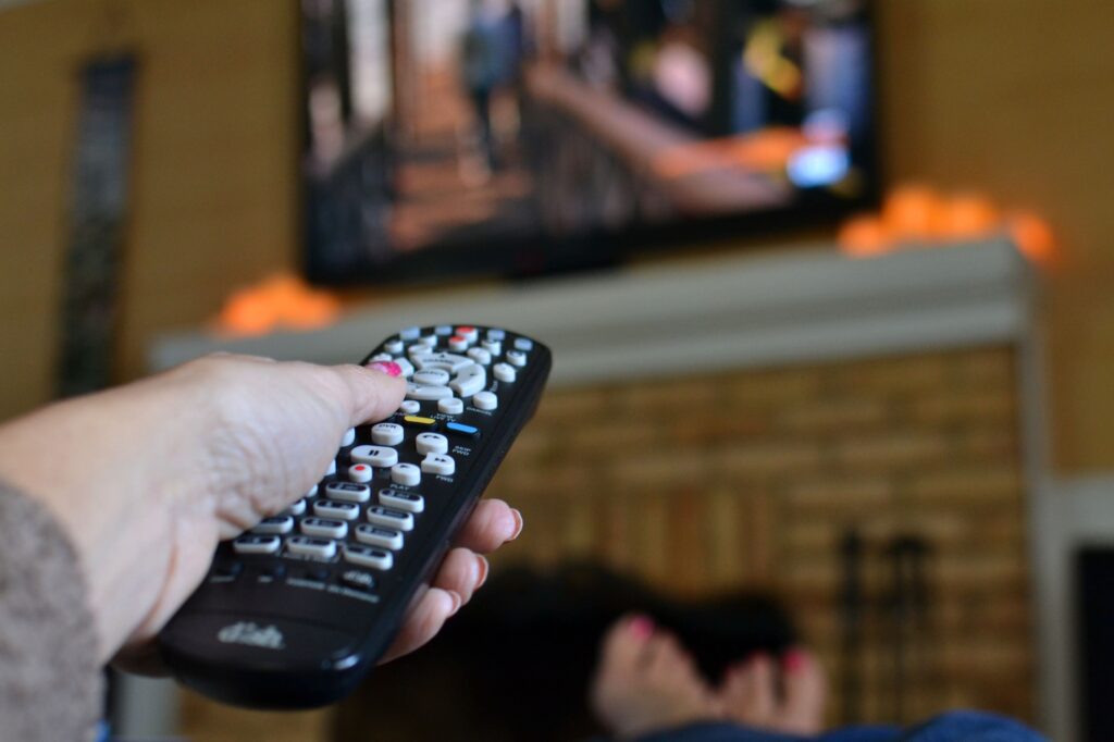 Woman holding a TV remote pointed at a big screen television while watching a movie or TV show.